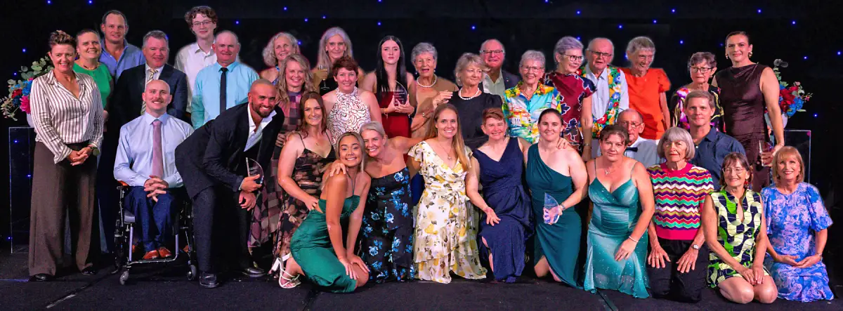 Large group of award recipients posing on stage, some holding trophies, at a formal awards event.